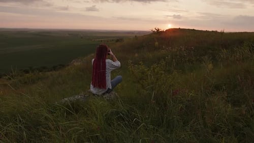 Woman with Dreadlocks Observes Sunset Landscape with Binoculars