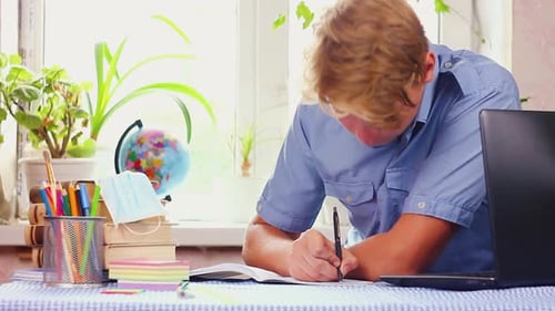 Student Writing in Notebook at Desk Indoors
