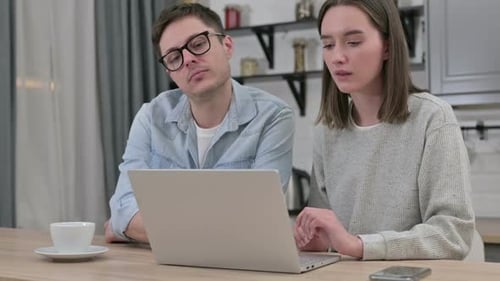 Jeune couple sérieux travaillant sur ordinateur portable dans le salon