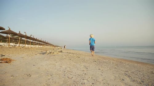 View of a Happy Boy Running Along the Beach Towards the Other Tourists