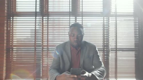 Man Uses Mobile Device in Sunlight-Filled Office