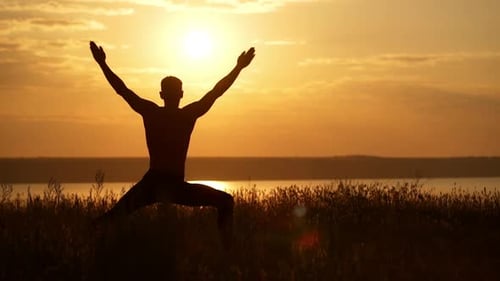 Silhouette of Young Sportive Man Practicing Yoga at Sunset