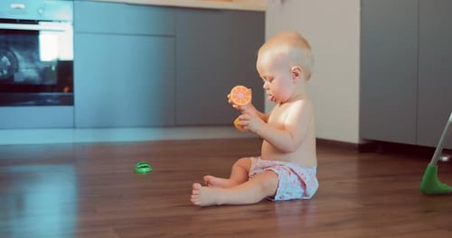 Blonde Haired Infant Playing with Toys on Kitchen Floor