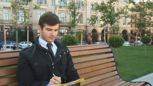 Young Man Writing on Bench in City Park