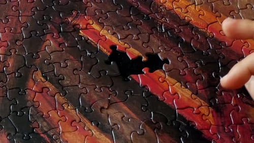 Die Hand einer Person, die die letzten Teile eines farbenfrohen Puzzles fertigstellt.