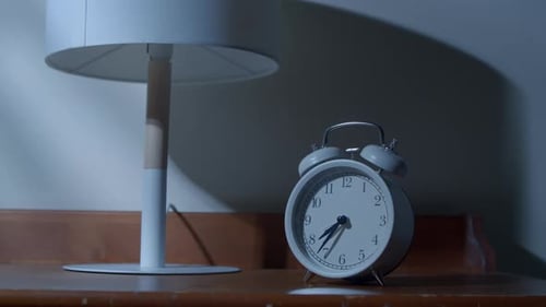 Hand Silencing Alarm Clock on Nightstand at Night