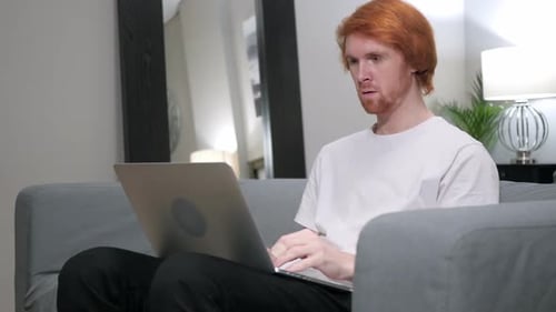 Excited Man Typing on Laptop on a Grey Couch