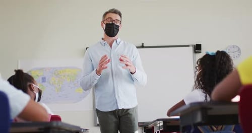 Caucasian male teacher wearing face mask teaching students in the class at school