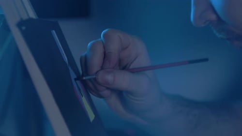 Busy Man Artist with a Brush in His Hand Picks Up an Oil Painting in a Cozy Studio. Talented Young