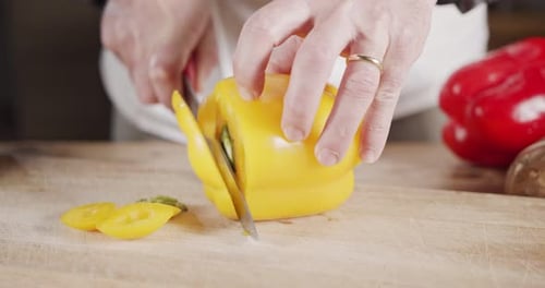 Slow motion close up of a chef knife slicing a yellow bell pepper