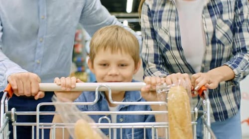 Boy Pushing Shopping Cart and Running with Parents in Supermarket