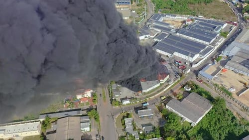 Aerial circling shot over black smoke column of burning warehouse