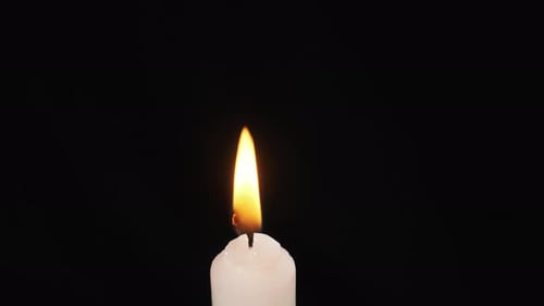 Une seule bougie est allumée sur fond noir. Éclairage. Flamme de bougie
