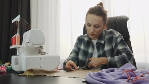 Woman working with fabric and scissor at the table in tailor's studio.