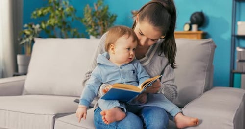 Mother Reading a Book to Her Infant on Couch