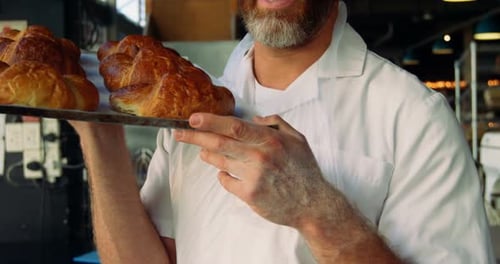 Male chef holding tray of croissants in bakery shop