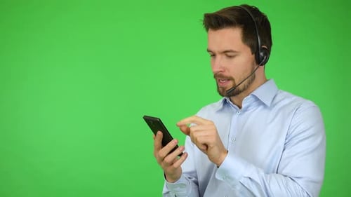A Young Call Center Agent Works on a Smartphone and Talks To a Caller, Then Smiles - Green Screen