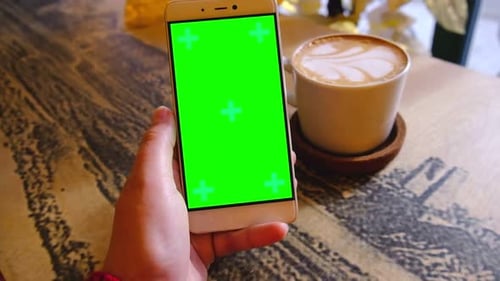 Person Holding Green Screen Phone with a Cup of Coffee on Table
