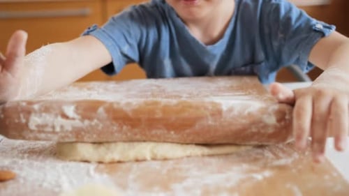 Child Using Rolling Pin to Flatten Dough Indoors