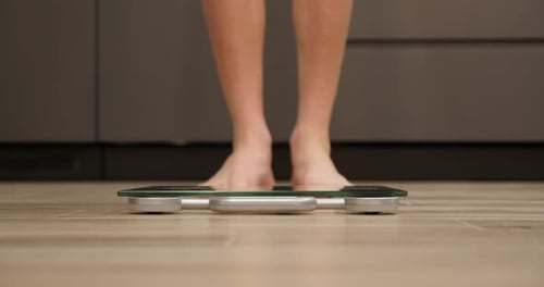 Male checking body weight on scales in kitchen.