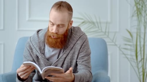 Bearded Adult Casually Reads a Book Indoors