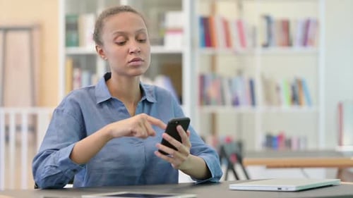 Serious African Woman Using Smartphone in Library