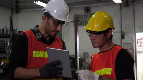 Two industrial workers using digital tablet, discussing work