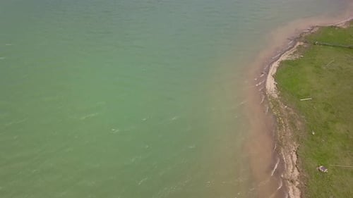 Aerial slowly panning showing the waves on water in lake / reservoir meeting with land