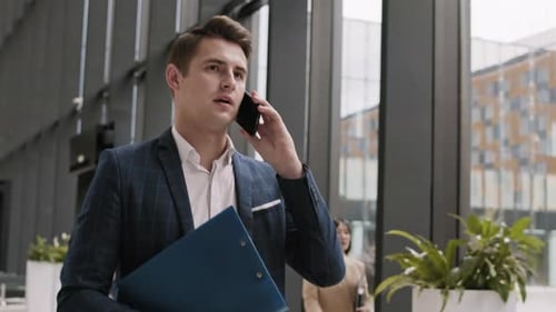 Businessman Walking and Talking on Smartphone in Office