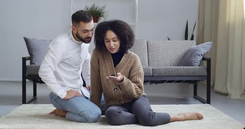 Couple Using Smartphone Together at Home on Carpet