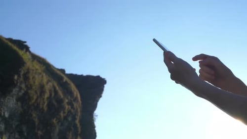 Hands Using Smartphone Near Rocky Cliff