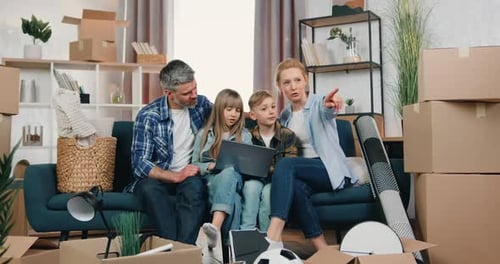 Familia sentada en el sofá entre cajas de cartón y discutiendo el diseño de la habitación