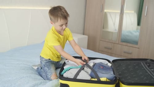 Little Boy Packing Bright Yellow Suitcase at Home