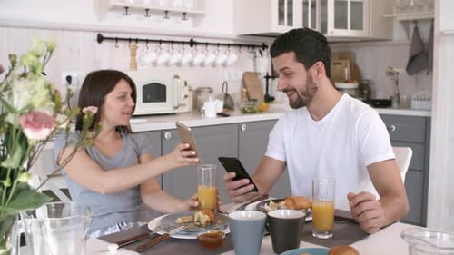 Couple Sharing Smartphones at Breakfast Table