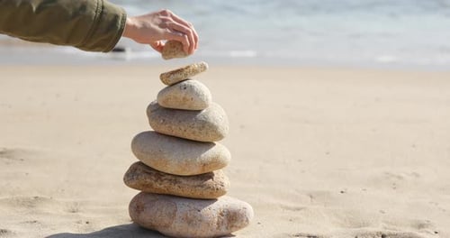 Frau Hand legt Kieselstein in Pyramide auf das Meer
