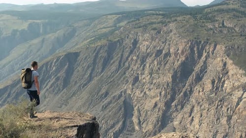 Happy Male Hiker Approaches the Edge of the Cliff and Raises His Hands Up Rejoicing in Success