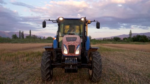 Blue Tractor Parked in Wheat Field at Sunset