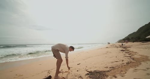 Vista circular de cerca de un joven hombre recogiendo la basura en una playa tropical de arena en Bali