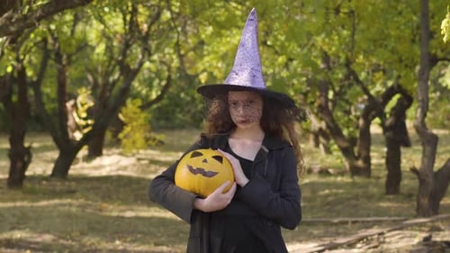 Cute Redhead Caucasian Girl Dressed in Halloween Witch Costume Standing in the Autumn Park. Child