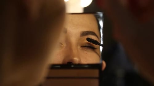 Woman Applying Mascara and Looking to the Mirror