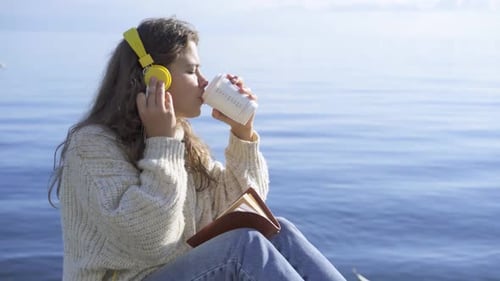 Woman Drinking Coffee Reading by Ocean