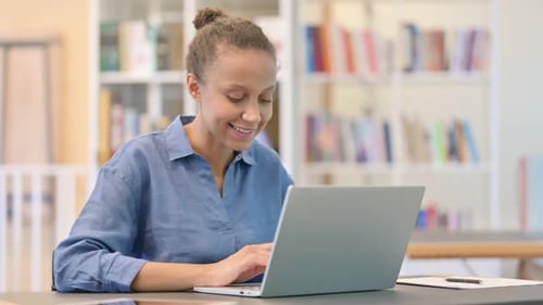 Cheerful African Woman Working on Laptop in Library