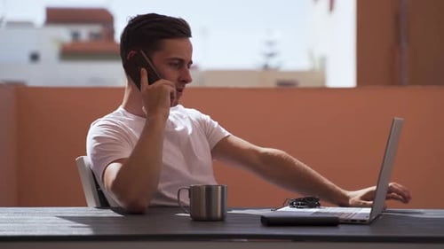 Young Man Working on Laptop, Talking on Phone