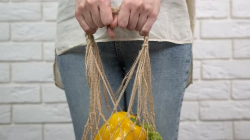 Woman Holds String Shopping Bag with Vegetables