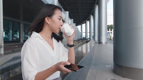Woman Using Phone and Drinking Coffee Outdoors
