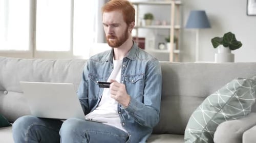 Man Using Laptop and Holding Card on Couch