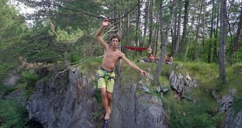 Un hombre trata de mantener el equilibrio mientras está holgazaneado en una cuerda floja en las montañas.