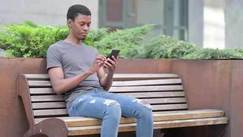 Junger Afrikaner benutzt Smartphone auf Bank