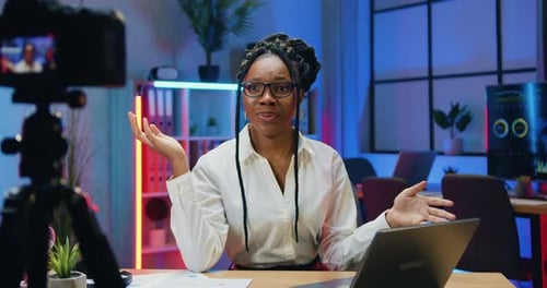 Empresaria con ropa elegante con gafas que está sentada frente a la cámara en la oficina por la noche