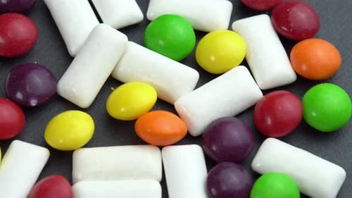 Sweets Colored Candies Skittles and Mint Chewing Pads Colored Sweets Rotate on a Black Plate